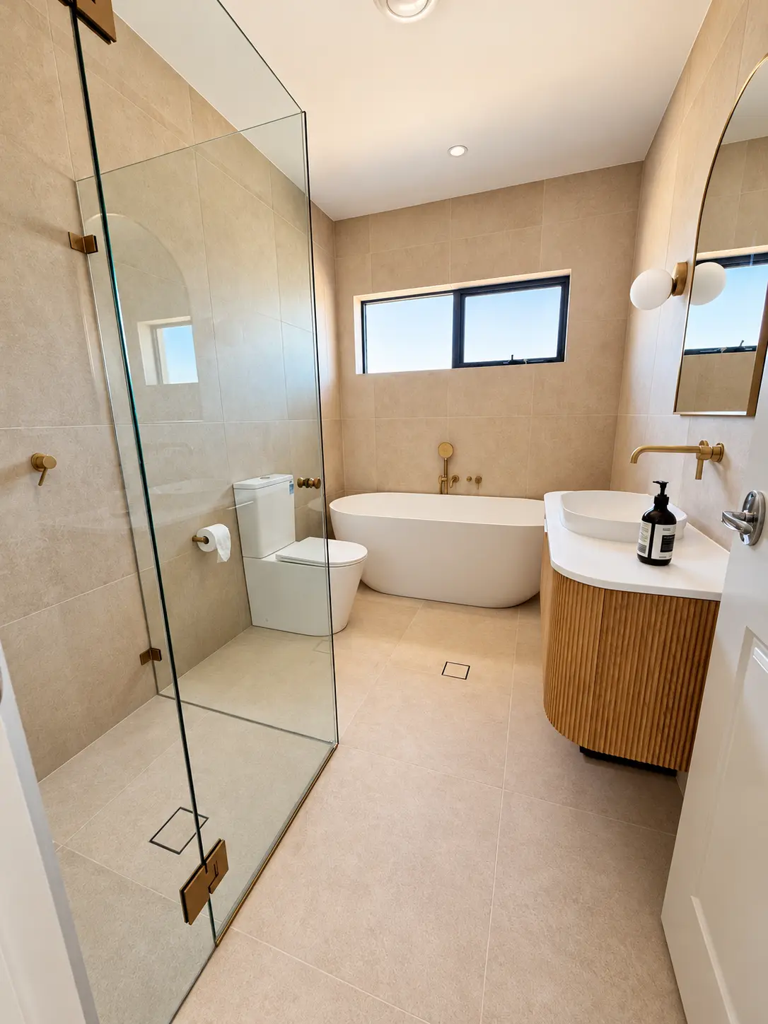 Natural stone-toned bathroom with freestanding bath and curved timber vanity